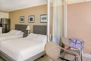 A hotel room with two beds, a chair, a table, and a refrigerator. - Quaint Studio in Heart of Waikiki (Honolulu)
