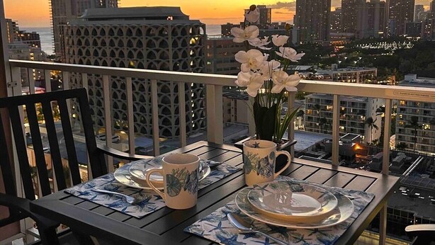 Une table dressée pour deux personnes, avec vue sur la ville au coucher du soleil, incluant des immeubles de grande hauteur et une étendue d’eau.