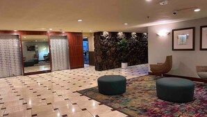 Un hall d’entrée spacieux avec un sol à carreaux, deux poufs verts, un tapis coloré, un mur en pierre et des tableaux encadrés accrochés au mur.