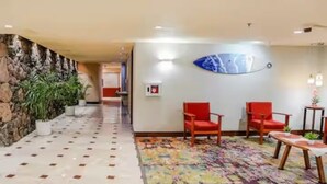 A hotel lobby with a stone wall, potted plants, a tiled floor, and two red chairs. - Dazzling Waikiki Studio+KIng Bed (Honolulu)