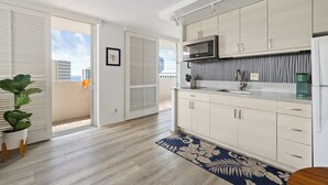 A modern kitchen with light wood cabinets, a stainless steel microwave, and a built-in oven. - Dazzling Waikiki Studio+KIng Bed (Honolulu)