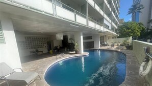 A swimming pool with lounge chairs and a covered area with tables and chairs.