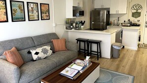 A modern living room with a grey sofa, a coffee table, and a kitchen area with white cabinets and stainless steel appliances.