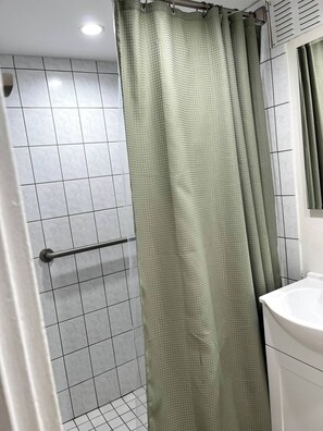 A bathroom with a shower area, tiled walls, a metal grab bar, and a white sink.