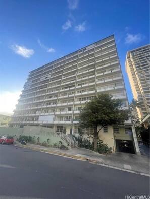 A multi-story building with a uniform facade, a visible entrance with a staircase, and a parked car in the foreground.