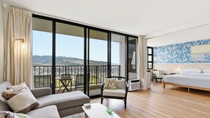 Een moderne hotelkamer met balkon, een bed, een bank, een klein tafeltje en uitzicht op de stad en de bergen.
