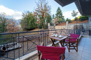 Una terraza con pared de piedra, mesa de madera y sillas rojas.