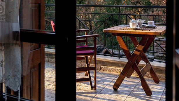 A balcony with a table and chairs, a view of trees and hills, and a window with curtains. - The Foxes - Modern 1BD apartment in the Forest

 (RPPV+R99 Potamia, Greece)