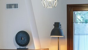 A fireplace with a visible fire, a floor lamp, and a window with a view of trees. - The Foxes - Modern 1BD apartment in the Forest

 (RPPV+R99 Potamia, Greece)