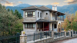 A two-story house with a balcony, stone walls, and a view of mountains. - The Foxes - Modern 1BD apartment in the Forest

 (RPPV+R99 Potamia, Greece)