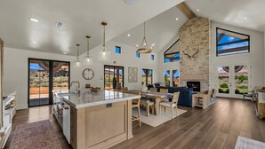 Une cuisine spacieuse dotée d’un îlot central, un coin repas avec des meubles en bois et un salon agrémenté d’une cheminée en pierre.