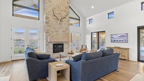 A spacious living room with a stone fireplace, large windows, and a high ceiling. - Zion Riverfront Farmhouse (Virgin)