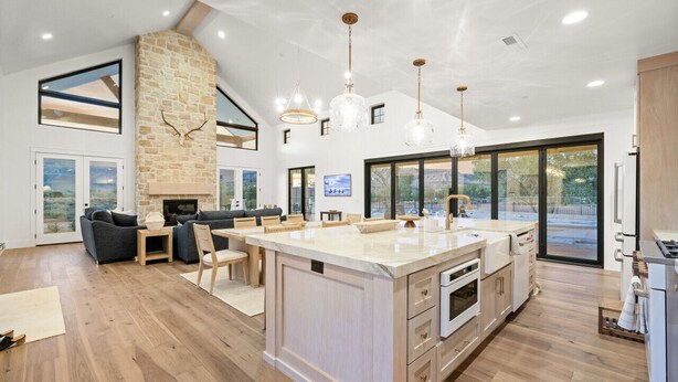 A spacious kitchen with a large island, modern pendant lights, and a stone fireplace. - Zion Riverfront Farmhouse (Virgin)