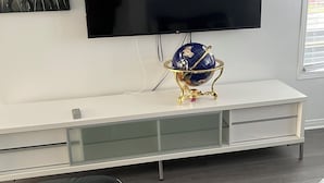 A modern living room with a flat-screen TV mounted on the wall, a glass-fronted entertainment unit, and a decorative globe on a gold stand. - Confortable Sunny Sky  (Gatineau)