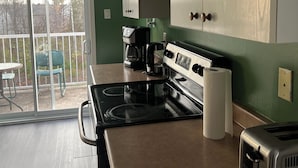 A kitchen with a stove, coffee maker, and toaster. There is a sliding glass door leading to a patio with chairs. - Confortable Sunny Sky  (Gatineau)