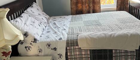 A bedroom with a bed, a nightstand, a lamp, and a window with curtains.