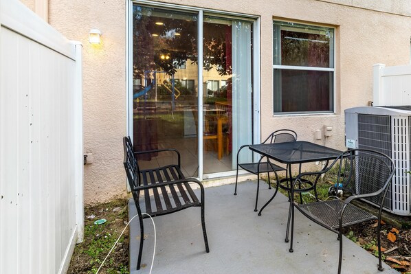 An outdoor patio area with a table and chairs, a sliding glass door, and an air conditioning unit.