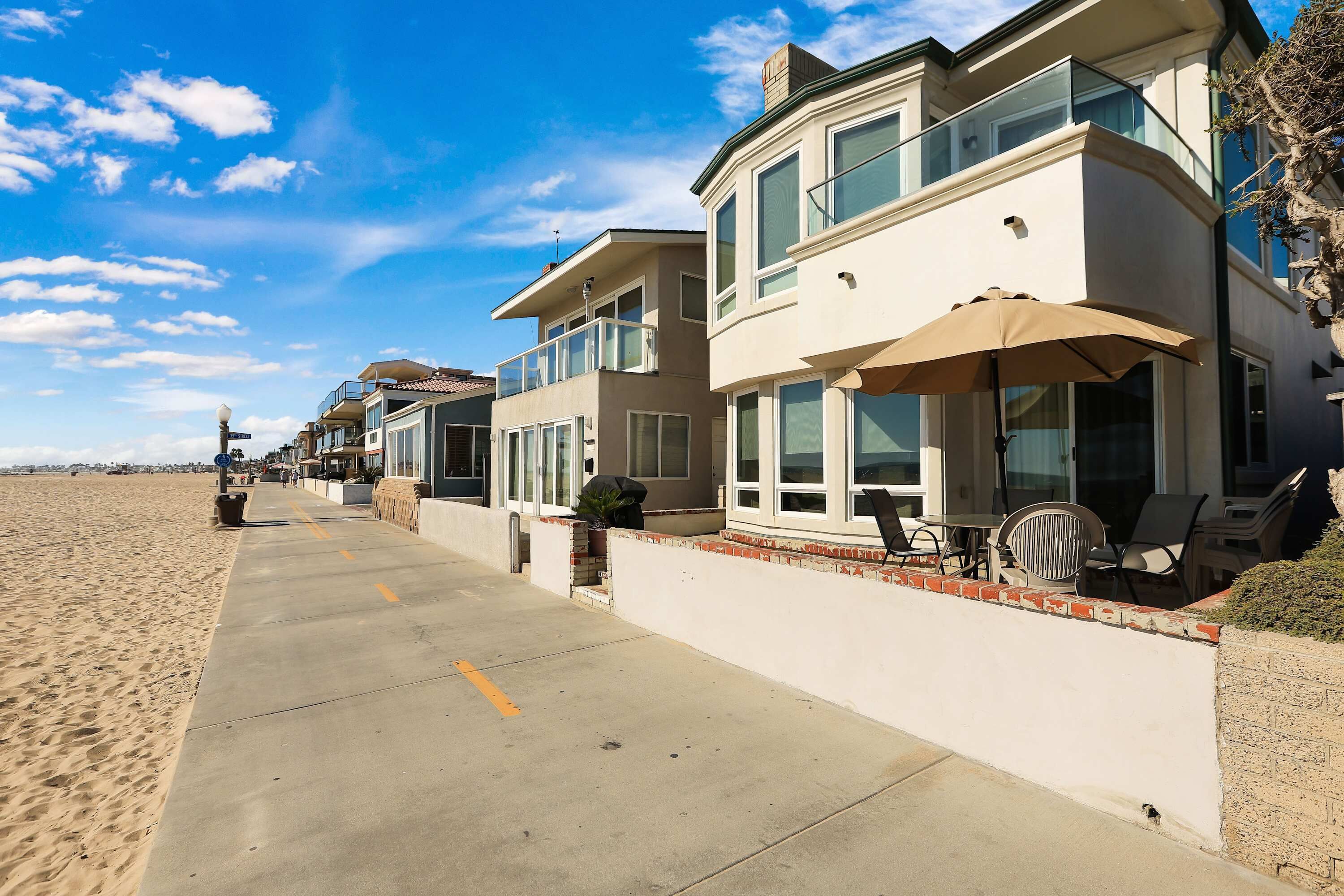 A beachfront property with a concrete walkway, a balcony with outdoor furniture, and a clear view of the beach.