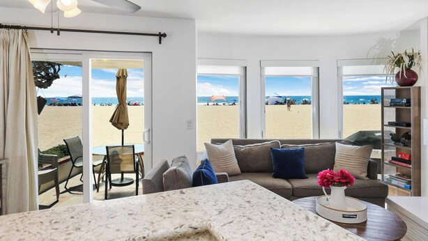Ein Wohnzimmer mit Blick auf den Strand, einem Deckenventilator und einem Bücherregal.