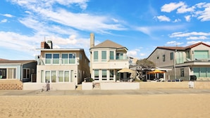 Ein Anwesen am Strand mit einem zweigeschossigen Haus, das große Fenster, einen Balkon und eine überdachte Terrasse bietet.