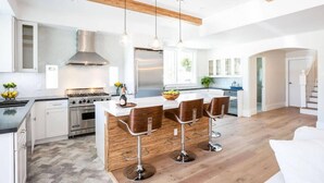 A modern kitchen with a central island, bar stools, stainless steel appliances, and wooden beams.