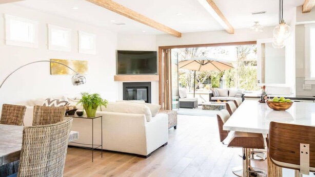A modern living room with a fireplace, a dining area, and a large window overlooking a garden.