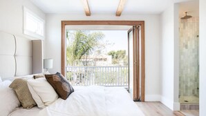 A bedroom with a large bed, a balcony with a glass door, and a shower area.
