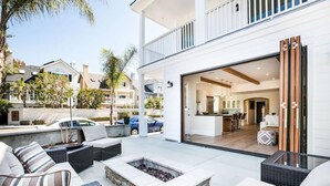 A modern outdoor living area with a fire pit, wicker furniture, and a view of the interior.