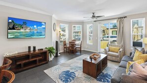 A living room with a large TV, a wooden entertainment unit, a coffee table, a sofa, and a dining area with chairs. - Newport Beach Retreat Steps to Sand, Boardwalk and Pier (Newport Beach)