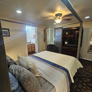 A bedroom with a bed, a sofa, a television, and a bathroom visible through an open door.