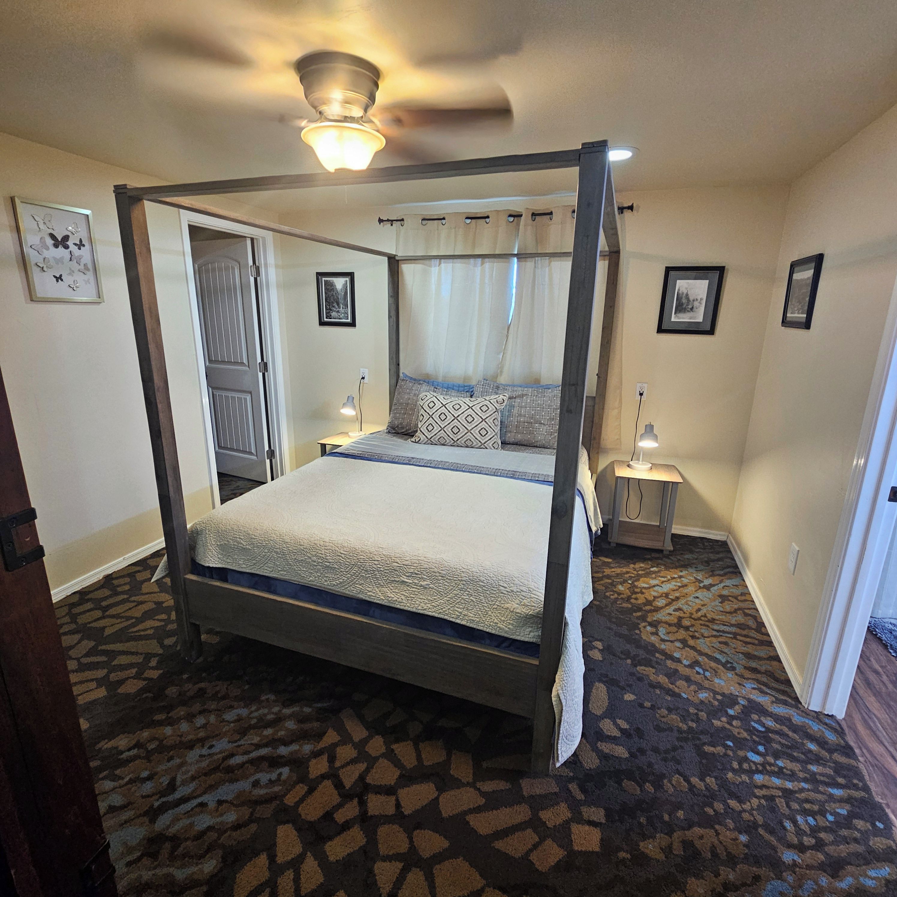 A four-poster bed with a canopy, a nightstand with a lamp, and a patterned carpet.