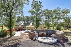 A circular outdoor fire pit area with a seating bench, surrounded by a stone wall. - Rural, high desert, private.  Hot Tub, fire pit, fully fenced, views for days! (Flagstaff)