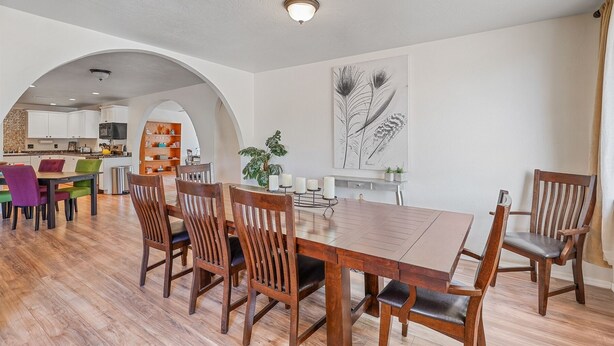 Un comedor amplio con una mesa y sillas de madera, una cocina al fondo e una gran impresión botánica en la pared.
