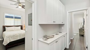 A bedroom with a bed, a ceiling fan, a window with blinds, and a hallway leading to a bathroom. - Newport Retreat B – Walk to Sand (Newport Beach)