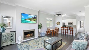 A spacious living room with a fireplace, a dining area, and a kitchen in the background. - Newport Retreat B – Walk to Sand (Newport Beach)