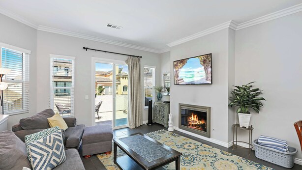 A living room with a sofa, a coffee table, a fireplace, and a large window with blinds. - Newport Retreat B – Walk to Sand (Newport Beach)