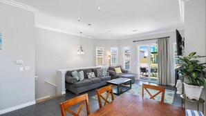 A modern living room with a grey sofa, a wooden dining table, and a large potted plant. - Newport Retreat B – Walk to Sand (Newport Beach)