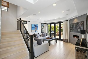 Un vaste espace de vie comprenant un escalier, une cheminée et une grande fenêtre donnant sur un jardin.