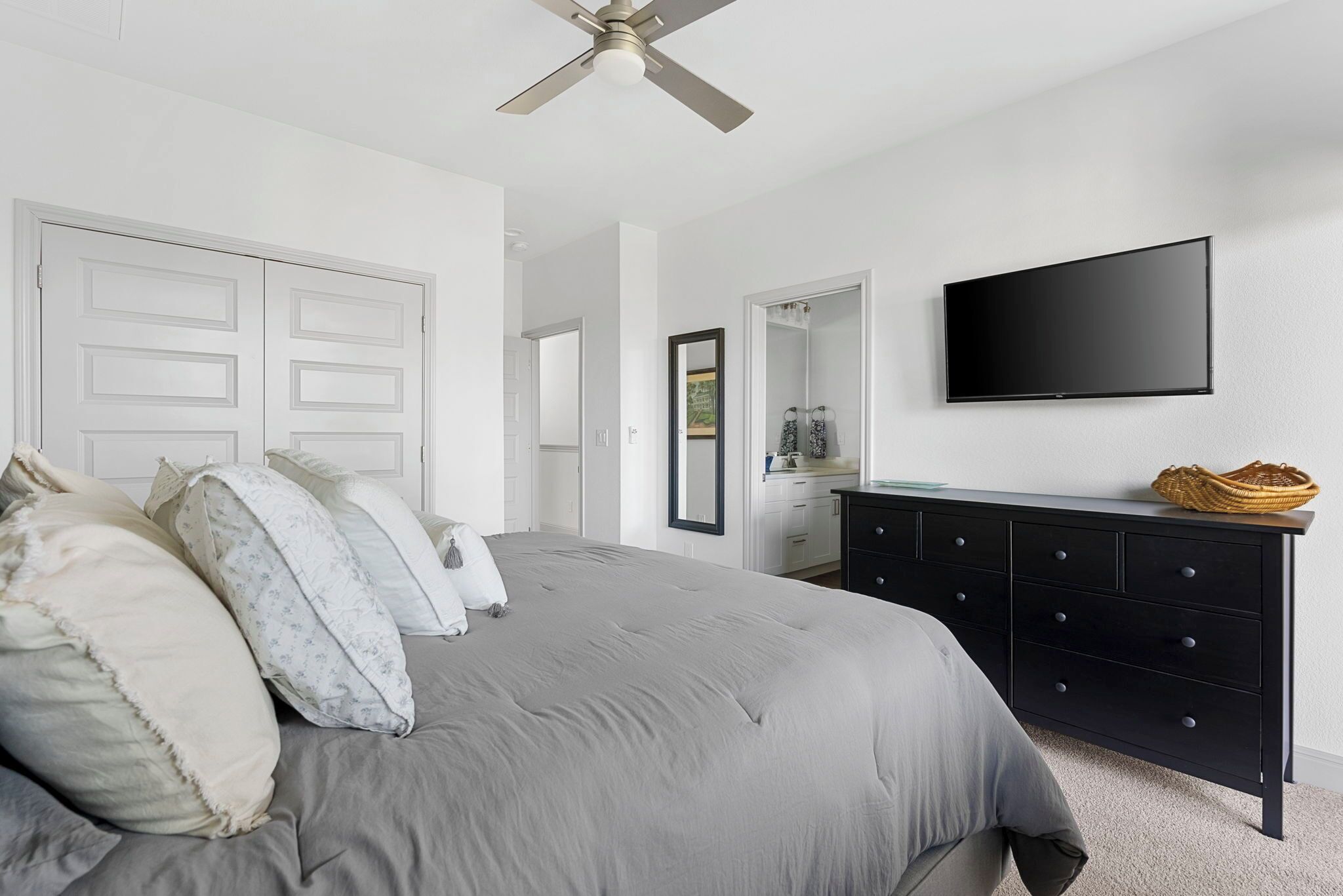 A bedroom with a bed, a dresser, a television, and a ceiling fan.