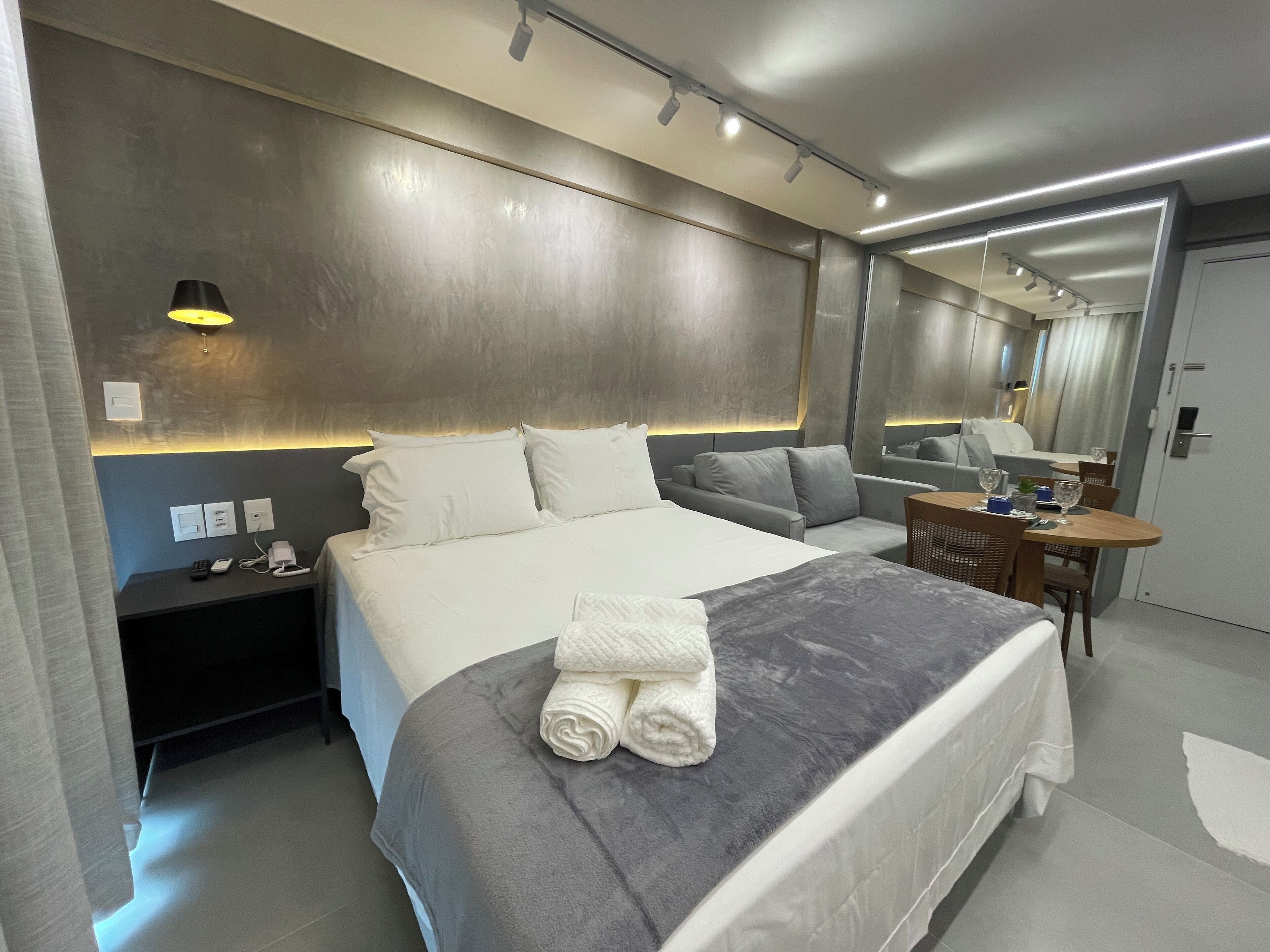 Ein modernes Hotelzimmer mit einem großen Bett, einem Nachttisch und einem kleinen Schreibtisch mit Stuhl.