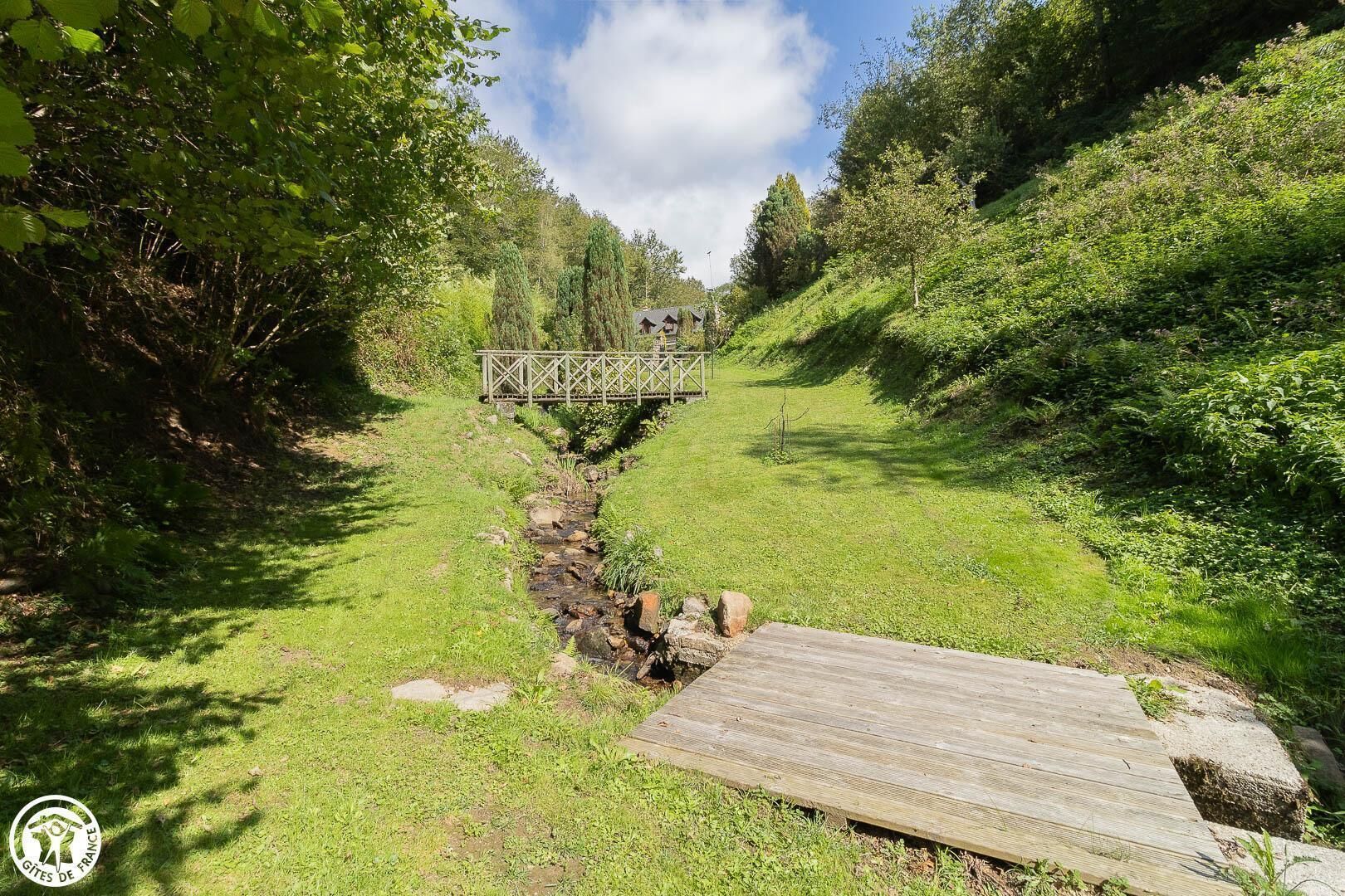 A wooden bridge over a stream in a lush green area with a clear sky.