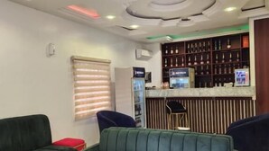 Een moderne hotel lobby met ruime groene banken, een marmeren bijzettafeltje en een bar met een wijnrek.