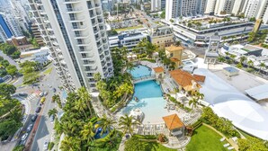 A high-rise hotel with a rooftop pool, palm trees, and a view of the cityscape. - 2 Bedroom 2 Bathroom Ocean View Unit at Chevron (CHEV 3204 - 3N - NB) (Surfers Paradise)