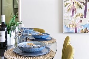 A dining table set with blue and white plates, glasses, and a bottle of wine, surrounded by woven placemats and a yellow chair.