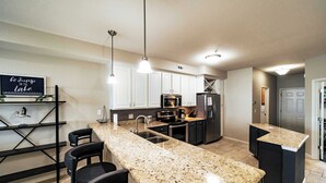 A modern kitchen with granite countertops, stainless steel appliances, and a bar area with stools. - Happy Haven @ Lands End – 3 BDR Resort Condo! (Osage Beach)
