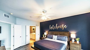 A bedroom with a large bed, a ceiling fan, a dark wall with the word "lakehouse" written on it, and a wooden floor. - Happy Haven @ Lands End – 3 BDR Resort Condo! (Osage Beach)