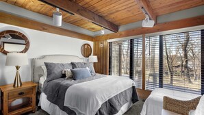 Ein Schlafzimmer mit einem großen Bett, Holzbalkendecke, einem Fenster mit Jalousien und einem Nachttisch mit Lampe.