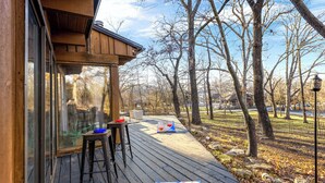 Eine Holzterrasse mit Glastrennwand, einem Tisch und einem Stuhl.