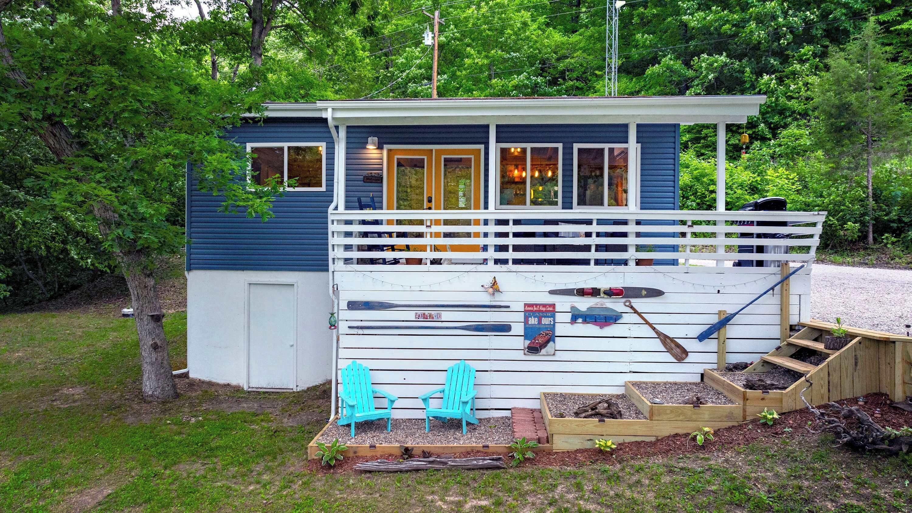 A cabin with a deck, two turquoise Adirondack chairs, and raised garden beds.