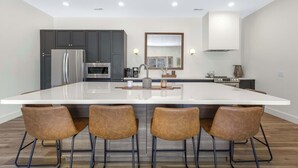 A modern kitchen with a large island, dark cabinets, stainless steel appliances, and four bar stools.